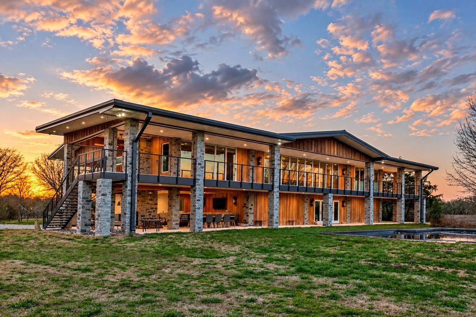 Barndominium built by Gehringer Construction, with stone columns and a covered balcony at sunset